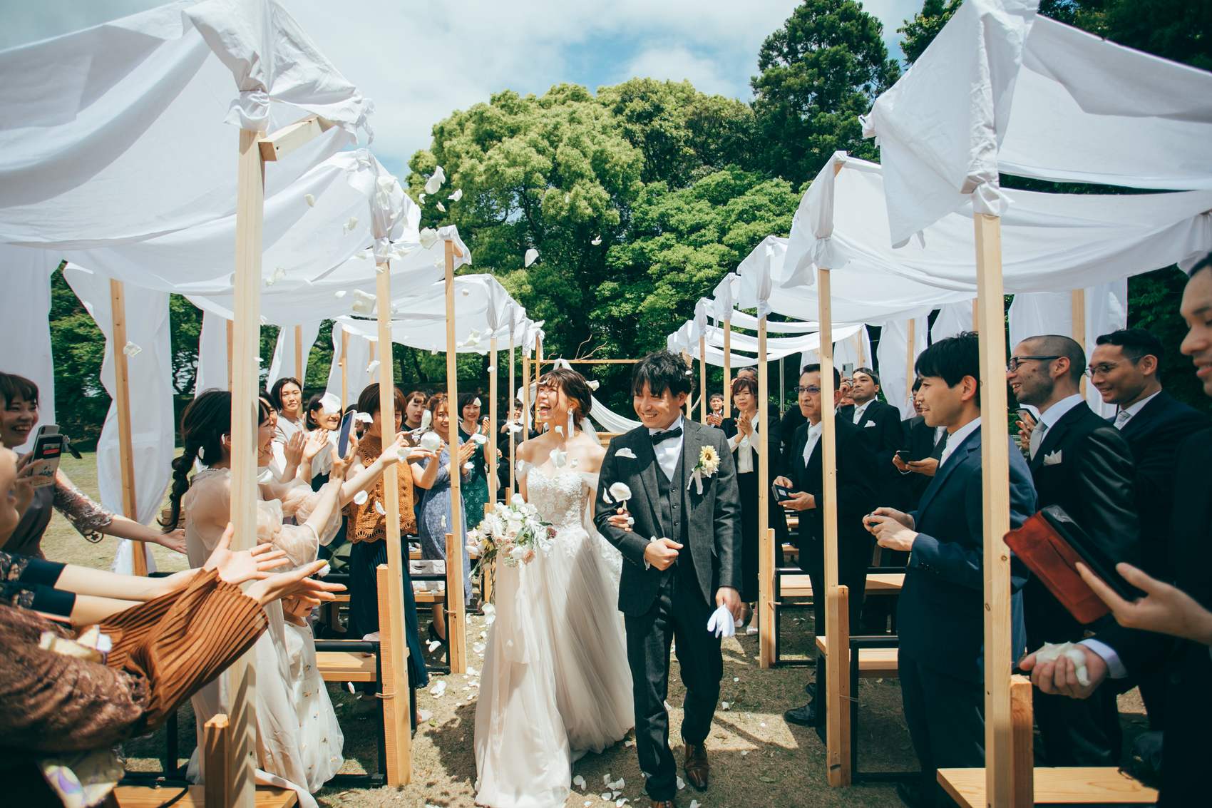 白いテントの下、ゲストの祝福を受けて歩く新郎新婦